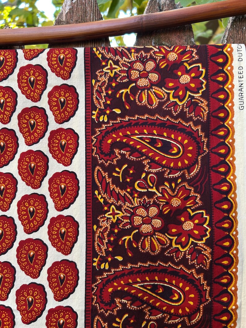 May include: A fabric with two distinct patterns. One side features a repeating pattern of red strawberry-like shapes on a white background. The other side showcases a paisley design in red, yellow, and brown. The text "GUARANTEED DUTCH" is visible.