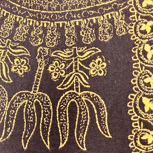 May include: Close-up of a brown fabric with a repeating yellow floral pattern. The design includes stylized flowers, curved shapes, and decorative borders. The fabric has a textured appearance.