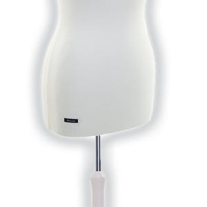 Könnte beinhalten: Eine weiße Torso-Schneiderpuppe mit glattem Stoffbezug, die vorne unten ein kleines schwarzes rechteckiges Etikett mit weißem Text aufweist. Die Schneiderpuppe wird von einer silbernen Metallstange und einem weißen hölzernen Dreifuß mit Kugelaufsatz getragen.