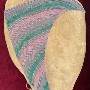May include: A crescent-shaped knitted shawl featuring alternating diagonal stripes of variegated green, pink, and grey yarn. The textile displays a consistent openwork stitch pattern throughout, creating a textured, lightweight appearance.