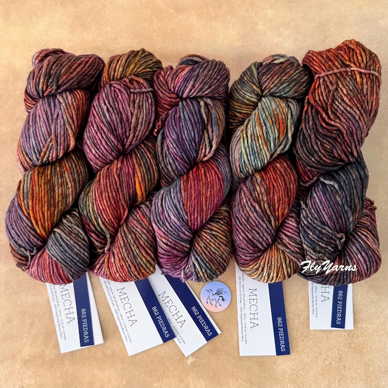 May include: Five skeins of Mecha yarn in the color 862 Piedras, featuring a variegated blend of deep purple, burnt orange, charcoal gray, and muted teal tones. Each skein includes a white paper label with the text Mecha and 862 Piedras.