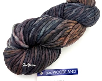 May include: A skein of super bulky Rasta yarn in a variegated blend of dark brown, charcoal gray, and muted teal tones. A white product label is attached, featuring the text 304 WOODLAND, RASTA, and technical specifications including 90 yd (82 m).