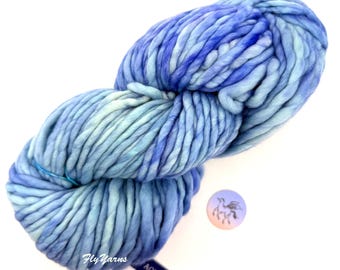 May include: A skein of thick, chunky yarn in a variegated blend of light blue, aquamarine, and deep royal blue tones. The yarn features a twisted texture and is labeled with the text Fly Yarns, Rasta, and Aquamarine, alongside a circular logo.