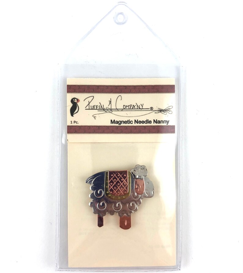 Pode incluir: Um porta-agulhas magn&eacute;tico de prata e cobre em forma de ovelha com uma sela marrom. A embalagem diz "Puffin Company" e "Magnetic Needle Nanny".