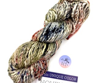 May include: A skein of Noventa yarn in a unique color blend. The yarn is a mix of cream, olive green, red, and black. A label with the text "101 Unique Color" and a logo is attached to the yarn.