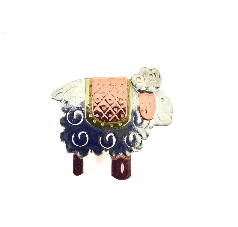 Profile of a sheep body made of recycled metal is etched with small swirls, eye and smile. Ears, feet and a blanket on the back made of copper. Blanket has a brass edging also etched with designs.