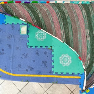 May include: A crescent-shaped knitted shawl featuring alternating wide bands of variegated forest green and muted mauve yarn. The shawl has a textured garter stitch pattern with subtle eyelet rows throughout, creating a soft, draped appearance.