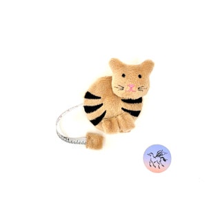 May include: A brown and black striped plush cat-shaped tape measure with a white tape and a pink nose.