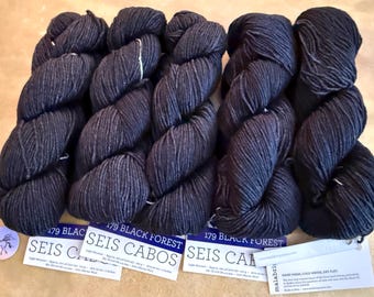 May include: Several skeins of dark blue yarn, labeled "179 Black Forest Seis Cabos." The yarn is tightly wound and has a textured appearance. The labels also include information about the yarn's composition and care instructions.