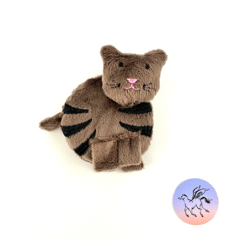 May include: A brown and black striped plush cat toy. The cat has a pink nose and black embroidered whiskers.