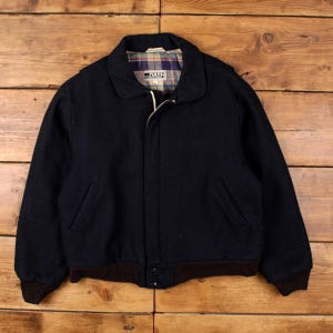 Op de afbeelding: Een marineblauwe jas met een bruine geribbelde zoom en manchetten. De jas heeft een kraag en twee voorzakken. De binnenvoering heeft een ruitpatroon. De merknaam "DASH" is zichtbaar op de voering.