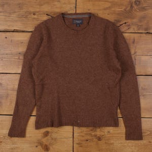 May include: A brown crew neck jumper with long sleeves. The jumper has a ribbed hem and cuffs. The brand name "Wallin" is visible on a small tag near the neckline. The jumper is made of a soft, textured material.
