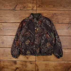 Puede incluir: Una chaqueta de camuflaje marrón, verde y negro con cierre de botones y un bolsillo con cremallera en el lado izquierdo.