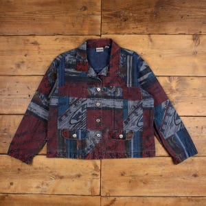 Puede incluir: Una chaqueta vaquera de manga larga con un diseño de parches en tonos rojo oscuro, azul marino y gris. La chaqueta tiene cuello, cierre frontal con botones de metal plateado y dos bolsillos delanteros con solapas abotonadas.