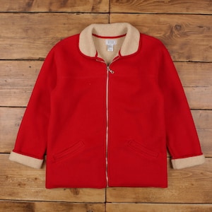 Könnte beinhalten: Eine leuchtend rote Fleecejacke mit cremefarbenem Sherpa-Kragen und -Bündchen. Die Jacke hat einen durchgehenden Reißverschluss und zwei Vordertaschen. Der Innenkragen hat ein kleines Etikett. Die Jacke wird auf einer Holzoberfläche präsentiert.