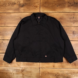 May include: A black Dickies zip-up work jacket featuring a classic collar, long sleeves with cuffs, and two front pockets. The jacket has a small Dickies logo patch on the lower left side and a quilted interior lining visible at the collar.