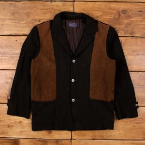 Könnte beinhalten: Schwarze Wolljacke mit braunen Wildlederpanels und drei Knöpfen. Die Jacke hat einen Kragen und geknöpfte Manschetten. Das Innenfutter ist gestreift. Der Markenname "Pendleton" ist sichtbar.