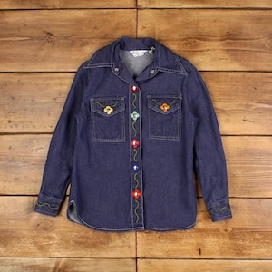 Op de afbeelding: Een donkerblauw denim shirt met lange mouwen en een knoopsluiting. Het shirt heeft kleurrijke geborduurde bloemen en knopen aan de voorkant.