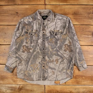 Puede incluir: Camisa abotonada de camuflaje con dos bolsillos en el pecho. La camisa presenta un estampado de hojas y ramas marrones, grises y beiges. La camisa de manga larga tiene cuello y cierres de botón. La camisa está hecha de tela duradera.