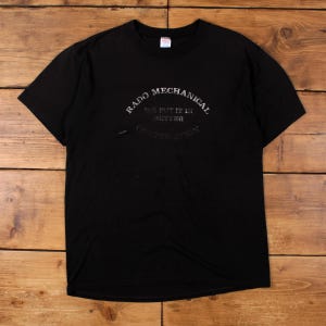 May include: Black t-shirt featuring the text "Rado Mechanical Corporation" in a curved layout, with "We put it in better" underneath. The shirt has a crew neck and is made of a soft fabric.