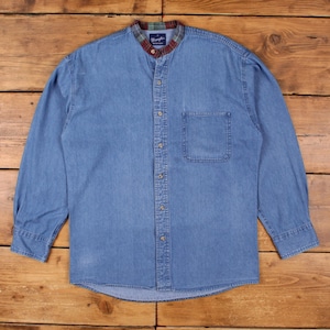 Puede incluir: Camisa vaquera azul claro con cuello mandarín y un bolsillo en el pecho. El cuello está adornado con un estampado de cuadros en tonos verdes, rojos y marrones. La camisa de manga larga tiene cierres de botón.