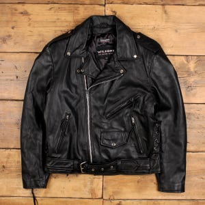 Könnte beinhalten: Schwarze Leder-Motorradjacke mit Reverskragen, asymmetrischem Reißverschluss und mehreren Reißverschlusstaschen. Die Jacke hat einen Gürtel in der Taille und die Marke "Wilsons" ist auf dem Etikett sichtbar.