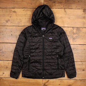 Könnte beinhalten: Eine schwarze Patagonia Kapuzenjacke mit Steppmuster, durchgehendem Frontreißverschluss und zwei seitlichen Reißverschlusstaschen. Das Patagonia Markenlogo ist auf der linken Brust und auf dem inneren Nackenetikett des Kleidungsstücks zu sehen.