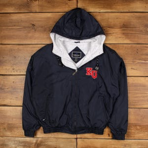 May include: Navy blue hooded jacket with a gray interior lining and a full zipper. The jacket features the letters "KU" in red on the front. The jacket has a drawstring hood and the brand name "Holloway" is visible on the label.