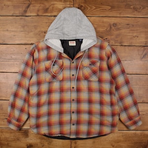 Puede incluir: Una camisa de cuadros con botones y capucha gris. La camisa presenta un estampado de cuadros rojos, naranjas y amarillos. Tiene dos bolsillos en el pecho y un forro negro. La capucha tiene un cordón.