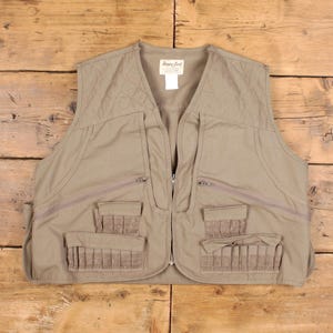 May include: A tan-colored vest with multiple pockets and a zipper closure. The vest has a quilted design on the shoulders and several pockets of varying sizes. The vest has the words "Happy Jack" on a tag.
