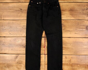 Puede incluir: Un par de pantalones vaqueros de mezclilla en color negro sólido con un diseño clásico de cinco bolsillos, cierre de botones y remaches metálicos en tono cobre en las esquinas de los bolsillos. Presentan un corte recto con costuras visibles.