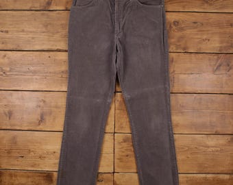 May include: A pair of gray corduroy pants with a classic five-pocket design. The pants have a button and zipper closure and belt loops. The corduroy fabric has a soft, textured appearance. The pants are laid flat on a wooden surface.