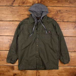 May include: An olive green work jacket with a grey hooded lining. The jacket features two chest pockets and two lower pockets, a button-up front, and a small Dickies logo patch. The hood has drawstrings.