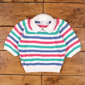 May include: A short-sleeved, striped sweater in white, pink, teal, and blue. The sweater has a white collar and is made of a knitted material. The stripes are horizontal and evenly spaced across the body of the sweater.