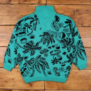May include: Teal-colored sweater with a high collar and a quarter-zip closure. The sweater features a black tropical design with palm trees, huts, and other island-themed elements. The sweater is made of a knitted material.