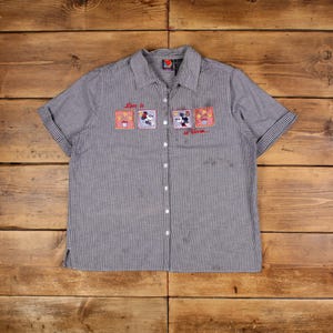 Peut inclure: Chemise à manches courtes à carreaux noirs et blancs. La chemise présente des écussons brodés avec Mickey et Minnie Mouse, et le texte "Love is in Bloom".