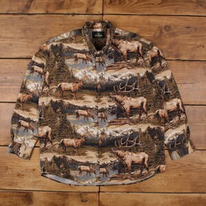 Puede incluir: Camisa abotonada de manga larga con un estampado de temática natural. La camisa presenta un diseño repetido de alces, montañas y árboles en tonos marrones, beige y verdes. La camisa tiene cuello y botones.