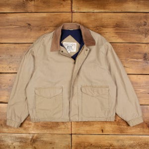 Puede incluir: Chaqueta beige con cuello marrón y forro interior azul marino. La chaqueta tiene dos bolsillos delanteros y cierre de cremallera. Fabricada con material duradero, ideal para climas más frescos.