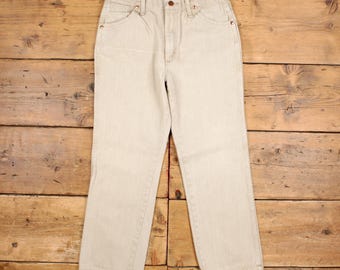 May include: A pair of light beige denim jeans featuring a high-waisted design, a button fly closure, five pockets, and copper-toned metal rivets. The pants have a straight-leg cut and a classic construction with visible stitching along the seams.