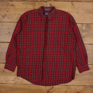 May include: A red plaid button-down shirt with long sleeves. The shirt features a classic plaid pattern in red, black, and white. The shirt is made of a soft, likely flannel material, and is laid flat on a wooden surface.
