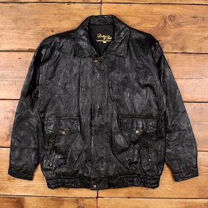May include: Black leather jacket with a collared neckline, two front pockets, and a button-up closure. The jacket has a textured, patchwork design and a ribbed hem. The label reads "Leather Club Genuine Leather".
