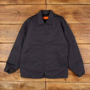 May include: A charcoal gray zip-up jacket featuring a classic collar, long sleeves with buttoned cuffs, and a small utility pocket on the left sleeve. The interior lining is a vibrant orange color, visible at the collar and the front zipper closure.