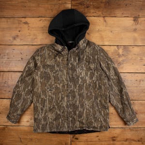 May include: A long-sleeve button-up shirt featuring a brown and tan camouflage pattern, a black attached hood with drawstrings, two chest pockets, and a quilted black interior lining. The garment has a front button closure and long sleeves.