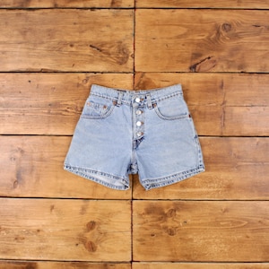 May include: Light blue denim shorts with a button fly and five pockets. The shorts are laid flat on a wooden surface.