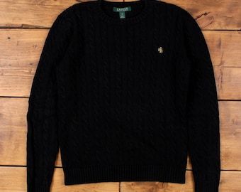 May include: Black cable-knit jumper with a crew neck. The jumper has a small gold logo on the chest and a brand label at the back of the neck. The garment is made of a thick, textured material.