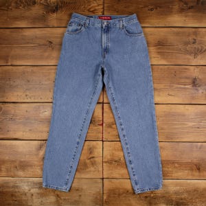 Op de afbeelding: Lichtblauwe spijkerbroek met een klassiek ontwerp met vijf zakken. De jeans heeft een rechte pijp en een knoop- en ritssluiting. Het kledingstuk wordt gepresenteerd op een houten oppervlak.