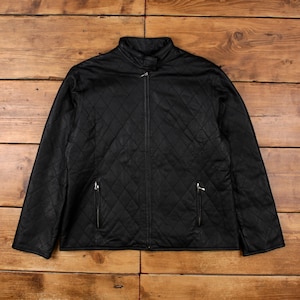 Może przedstawiać: Czarna pikowana kurtka z rombowym wzorem. Kurtka ma stójkę, zamek błyskawiczny na całej długości i dwie kieszenie zapinane na zamek. Kurtka jest wykonana z gładkiego, prawdopodobnie skóropodobnego materiału.