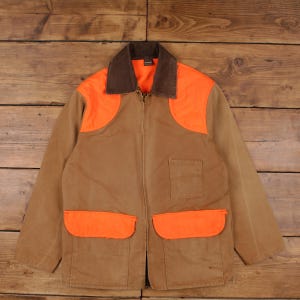 May include: A brown and orange hunting jacket with a brown corduroy collar, orange shoulder patches, and two orange front pockets. The jacket has a zipper closure and a single square pocket on the chest.