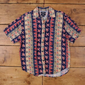 May include: Short-sleeved button-down shirt with a colorful geometric pattern. The shirt features a navy blue background with red, beige, and light blue floral and triangular designs. The shirt has a collared neckline and a button-up front.