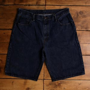 May include: Dark blue denim shorts with a button closure, pockets, and belt loops. The shorts are made of a sturdy denim material and have a classic, casual style. The shorts are laid flat on a wooden surface.